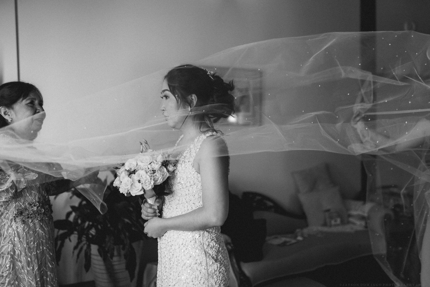 A bride and groom share an intimate moment during their wedding ceremony with flowing veil in black and white.