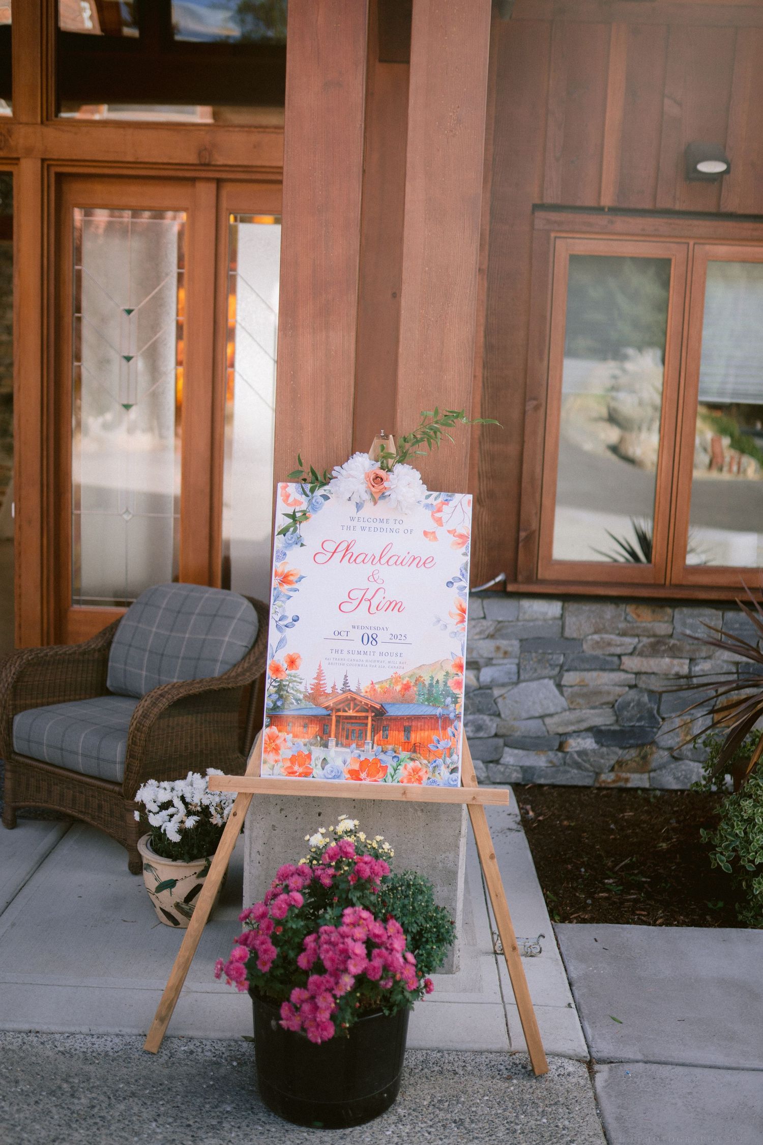 Pink floral welcome signs displayed on wooden easels with potted flowers at an outdoor venue entrance.