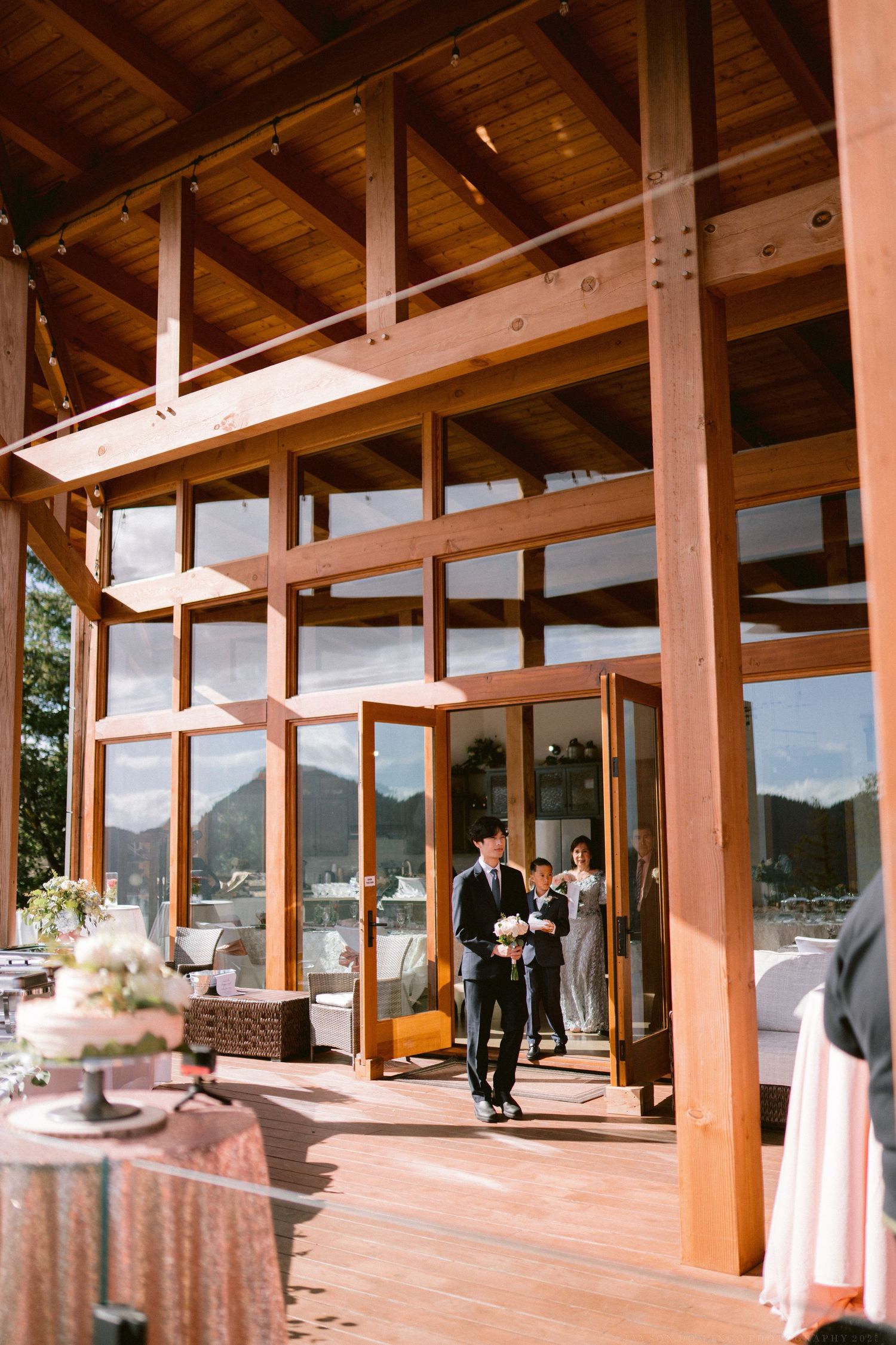 Spacious reception venue with exposed wooden beams and panoramic windows showing mountain landscape.