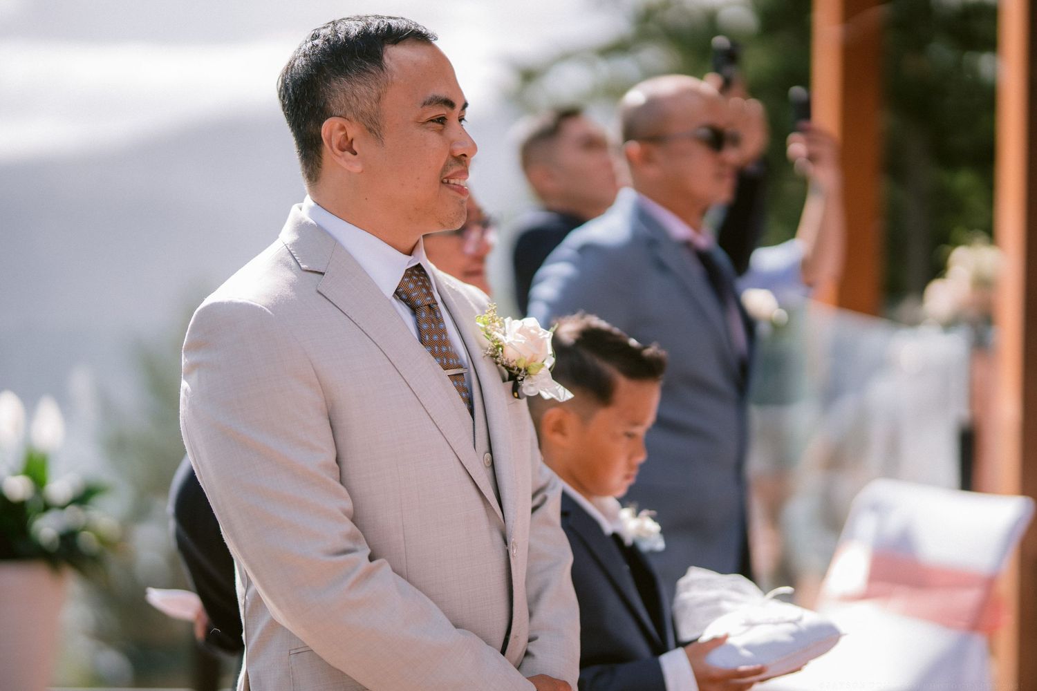 Wedding guests in formal attire gathered at an outdoor ceremony venue.