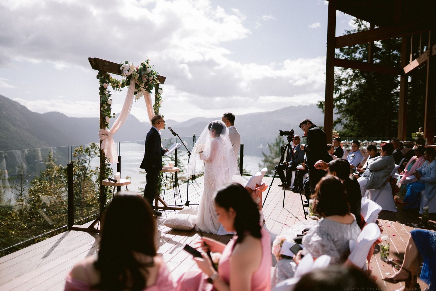 Outdoor wedding ceremony with mountain views and guests seated in white chairs.