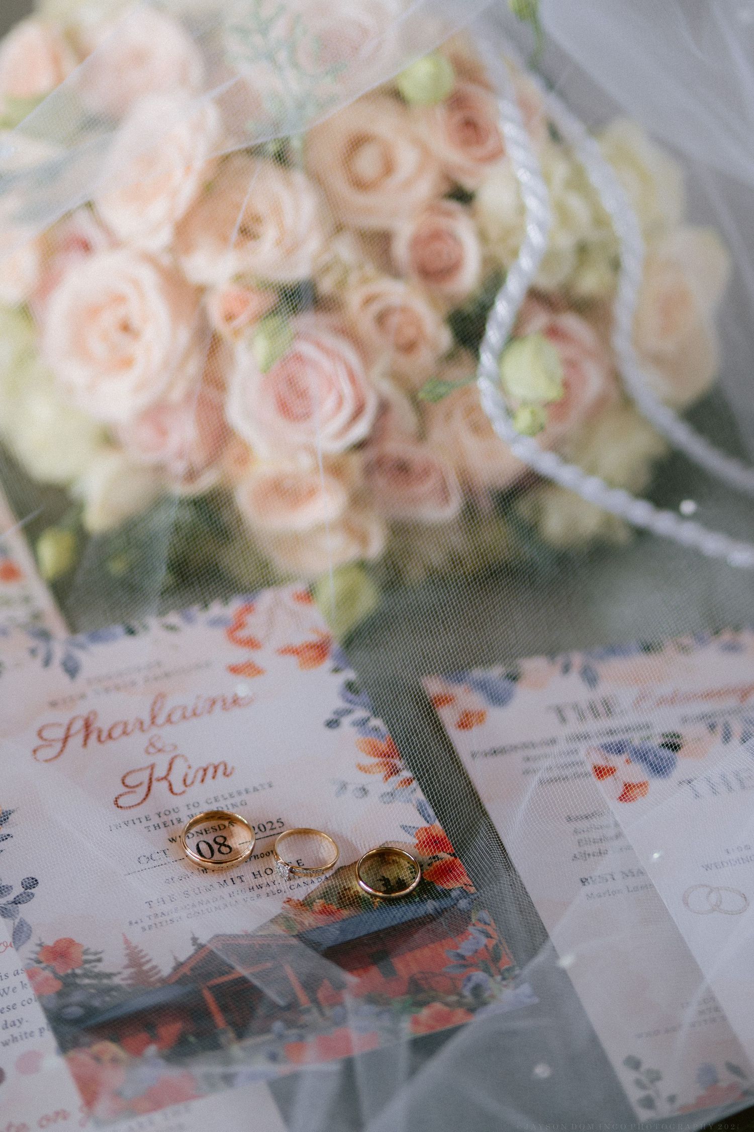 Wedding invitations with delicate pink roses and gold rings displayed on a light surface.