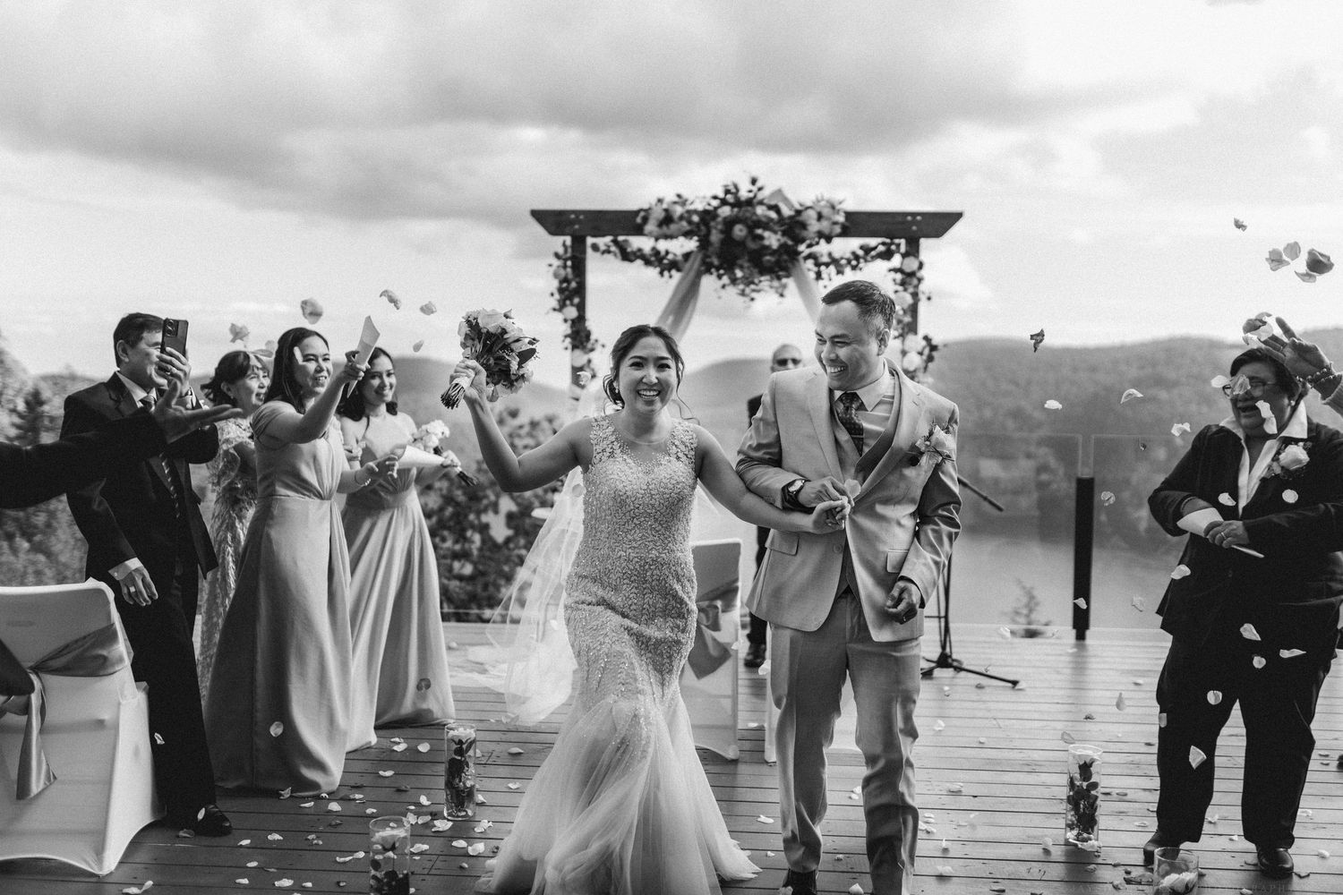 Black and white photo of wedding guests celebrating outdoors under cloudy skies.
