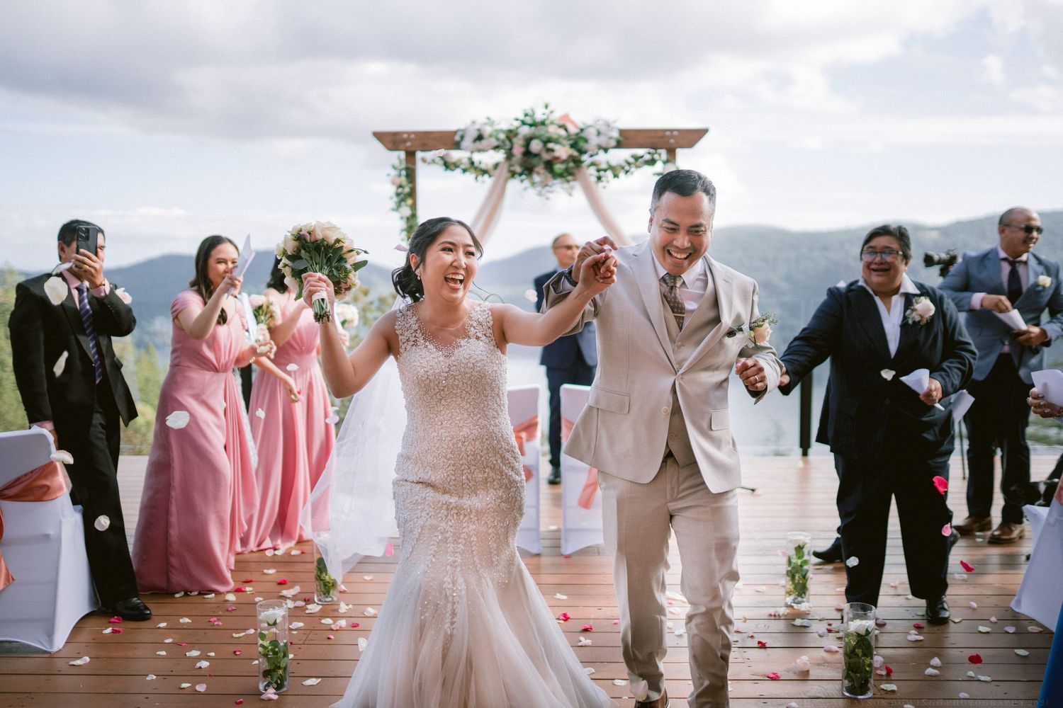 Wedding party celebrating and dancing together on a lakeside deck during a summer reception.