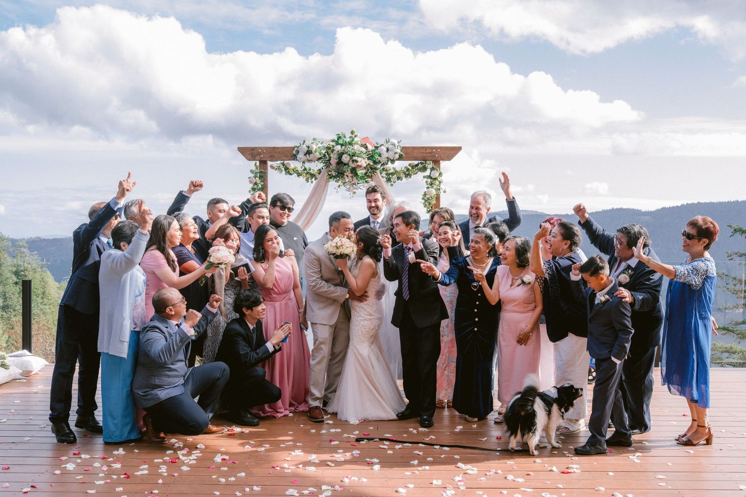 A group of wedding guests celebrate outdoors by throwing flower petals during a joyful beach ceremony.
