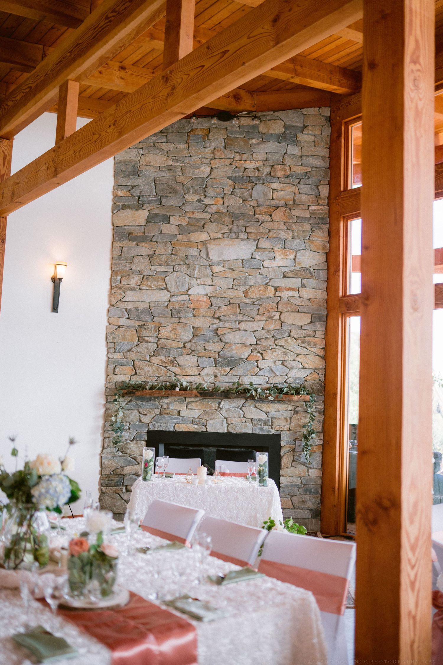 Elegant wedding reception tables set with white linens and floral centerpieces against a rustic stone wall interior.
