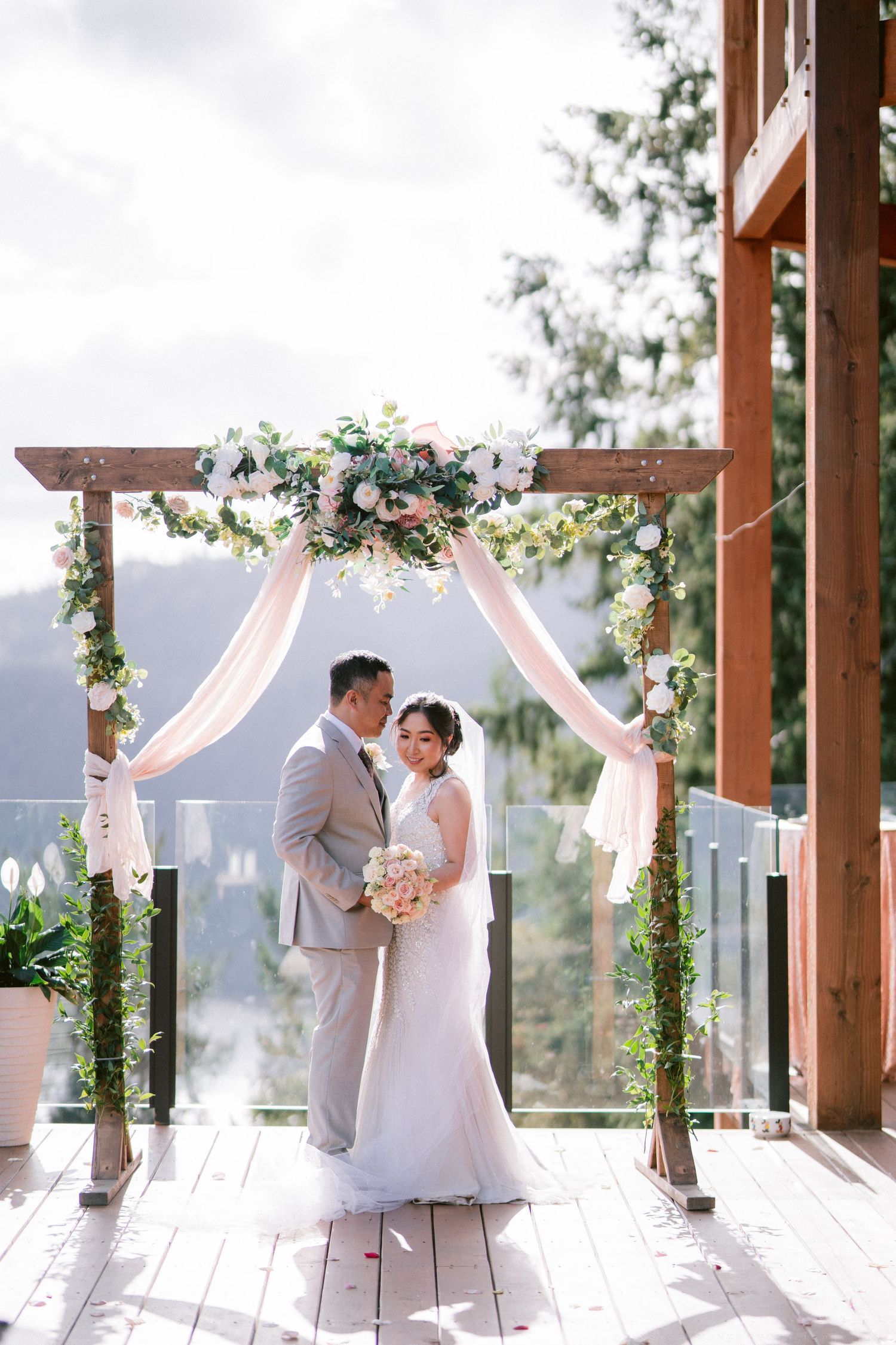 Romantic wedding ceremony setup with draped floral arch overlooking mountain landscape.