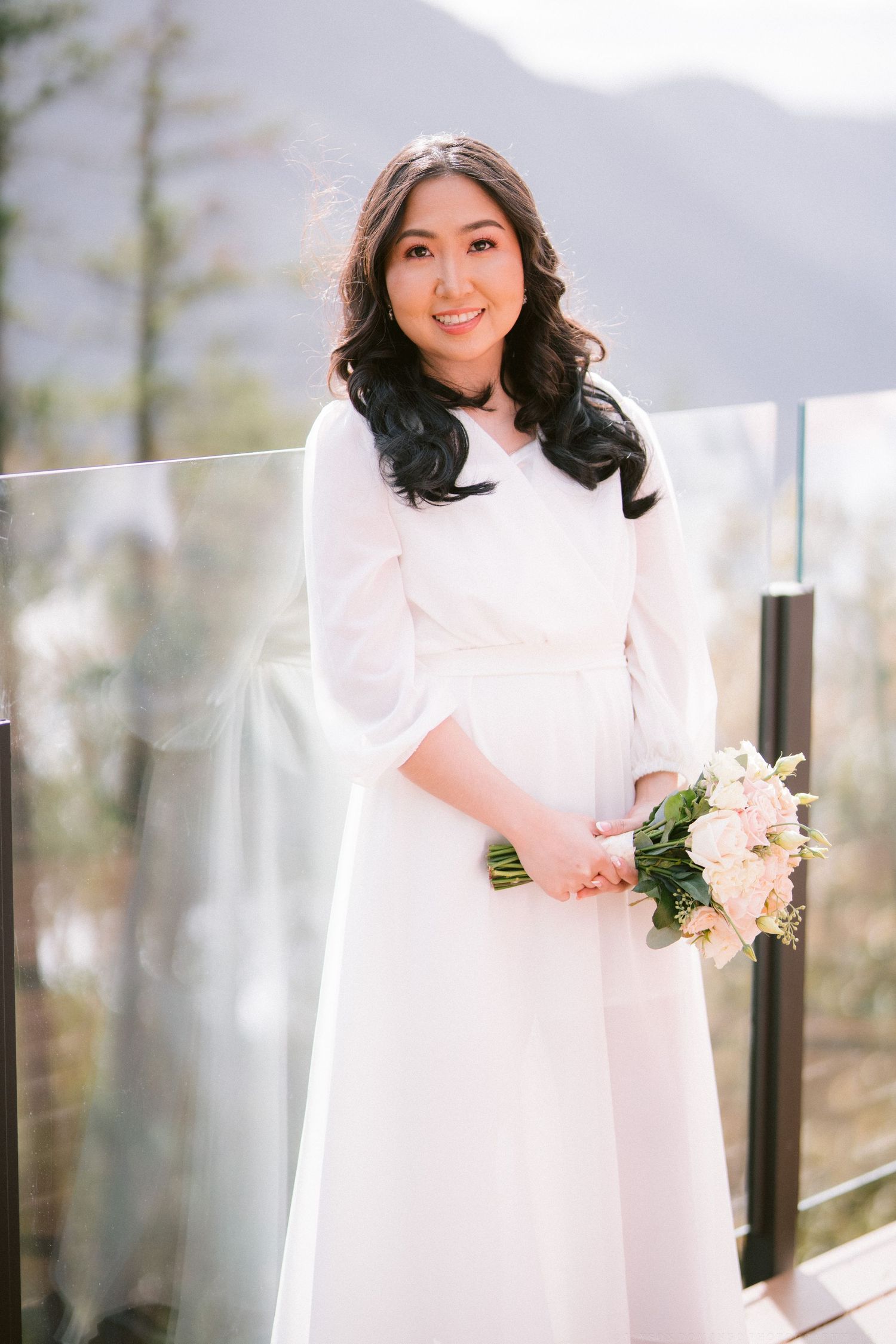 A person in a white winter coat holds a delicate bouquet of pink roses against a mountain backdrop.