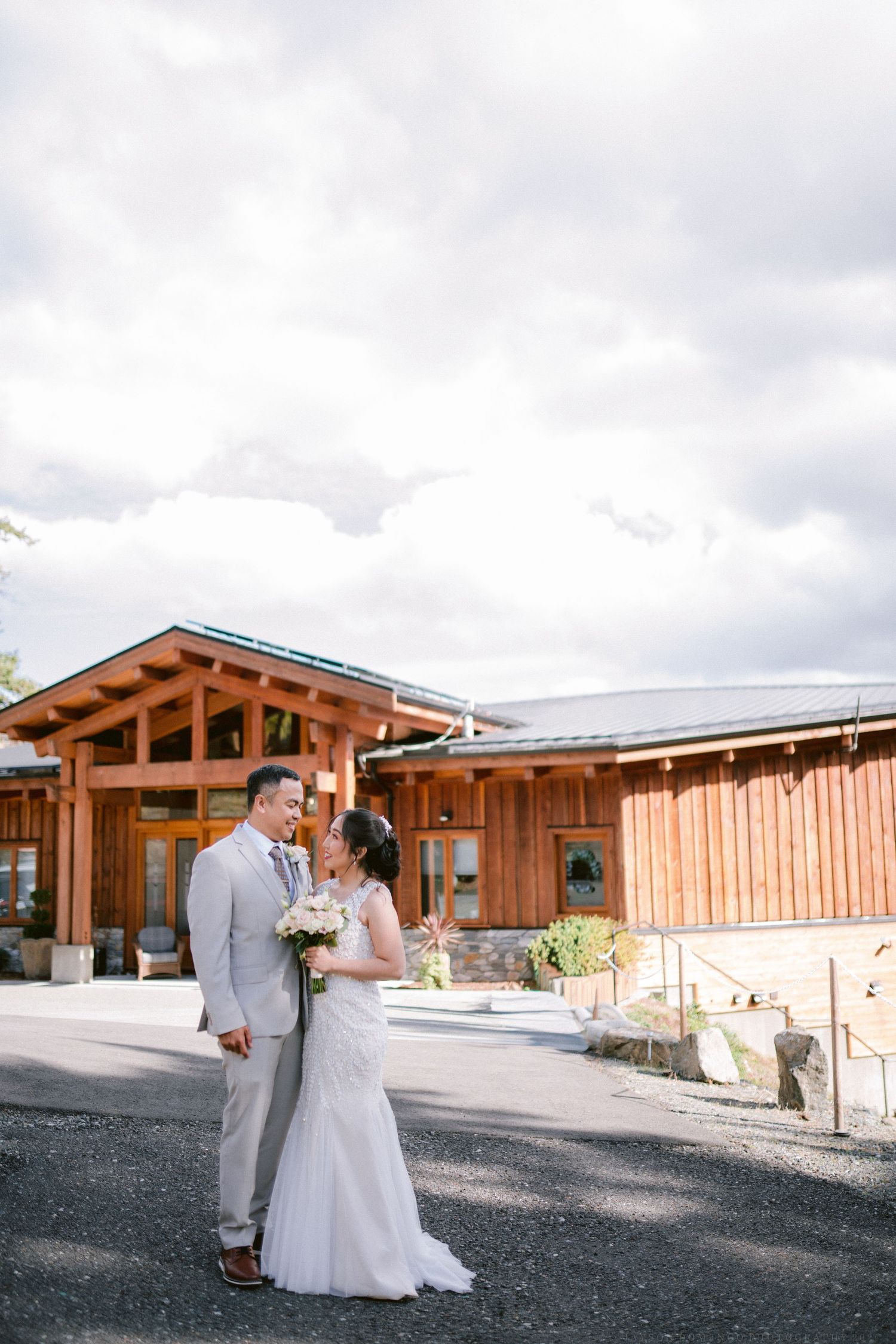 Rustic wooden lodge venue with newlyweds posing outside on a cloudy day.