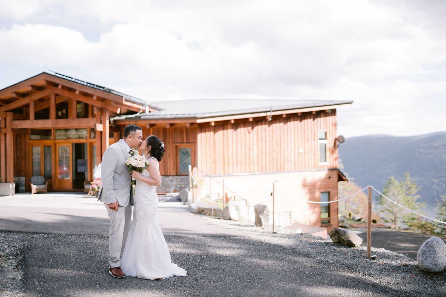 Newlyweds share a moment outside rustic mountain venue with scenic views.