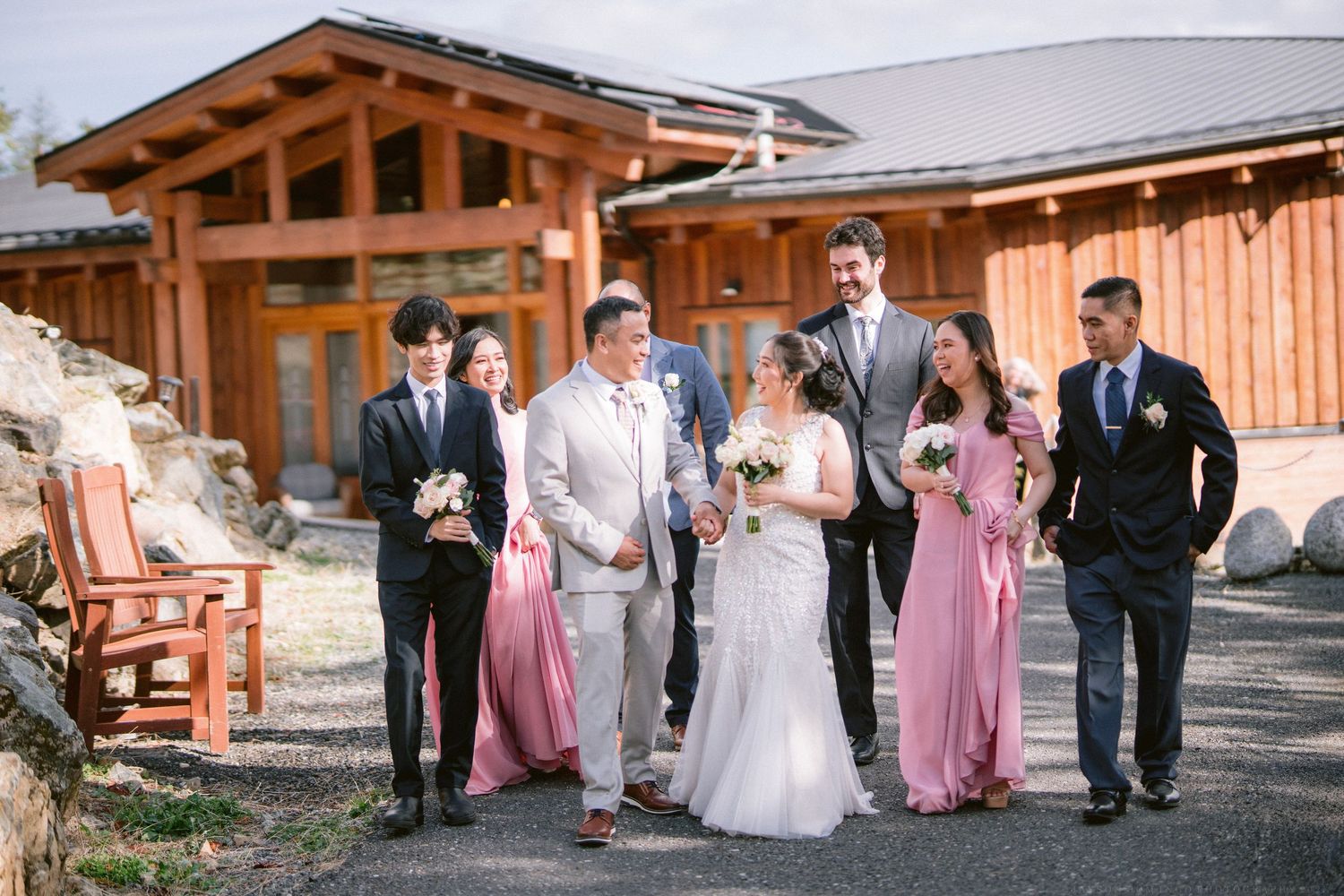 Wedding party walks together outside rustic wooden lodge wearing pink and gray attire.
