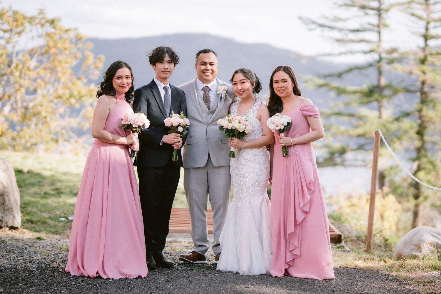 Wedding party in pink and gray attire poses together against scenic mountain backdrop during golden hour.