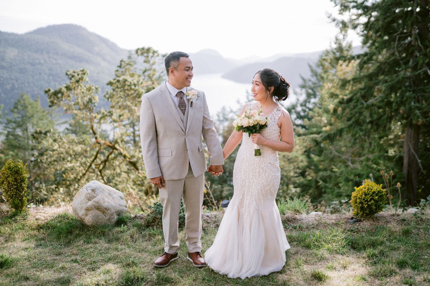 A romantic wedding couple poses together on a mountain overlook with scenic views in the background.