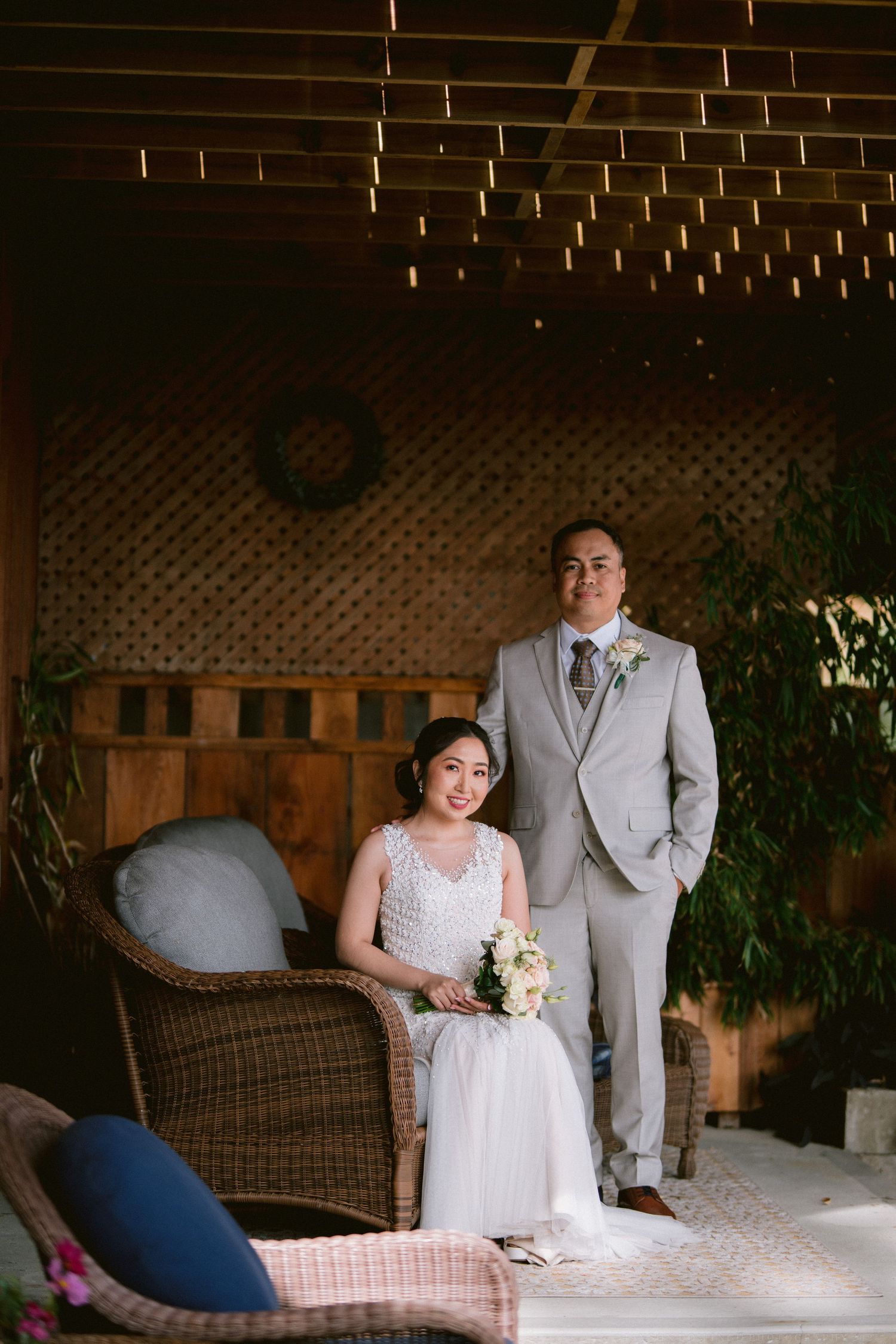 A wedding couple poses on indoor wicker furniture with soft lighting and decor.