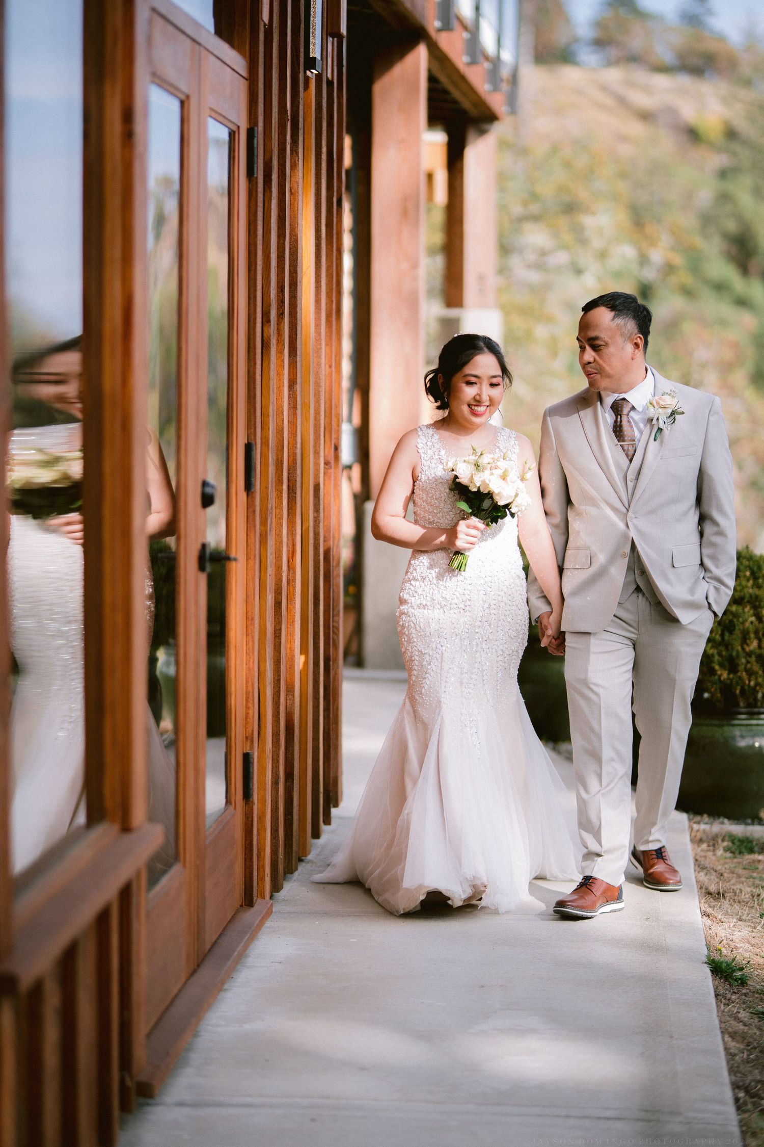 Elegant couple walks along covered walkway of mountain venue in formal wedding attire.