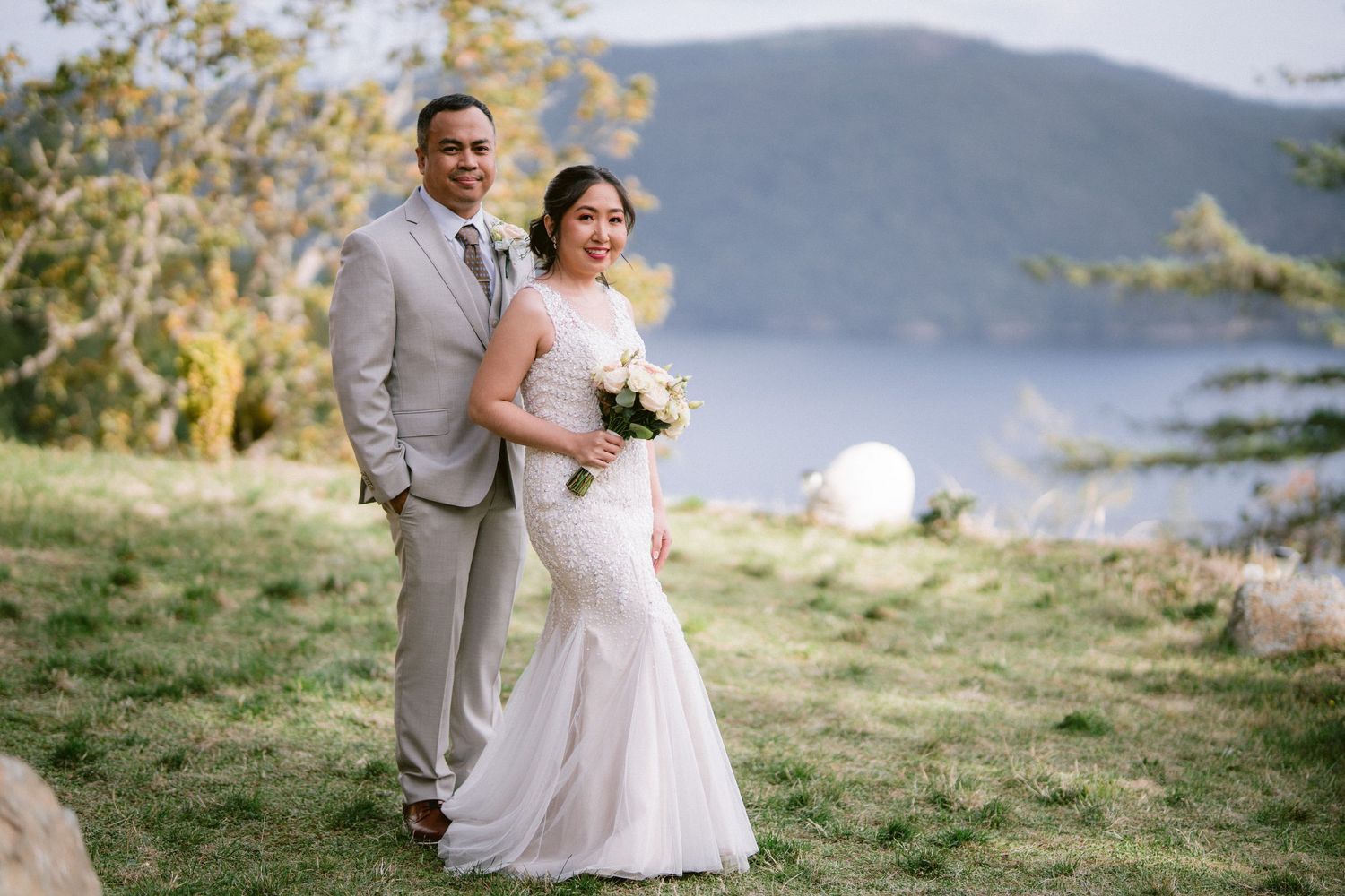 Wedding celebration on a grassy hillside overlooking a serene lake and mountains.