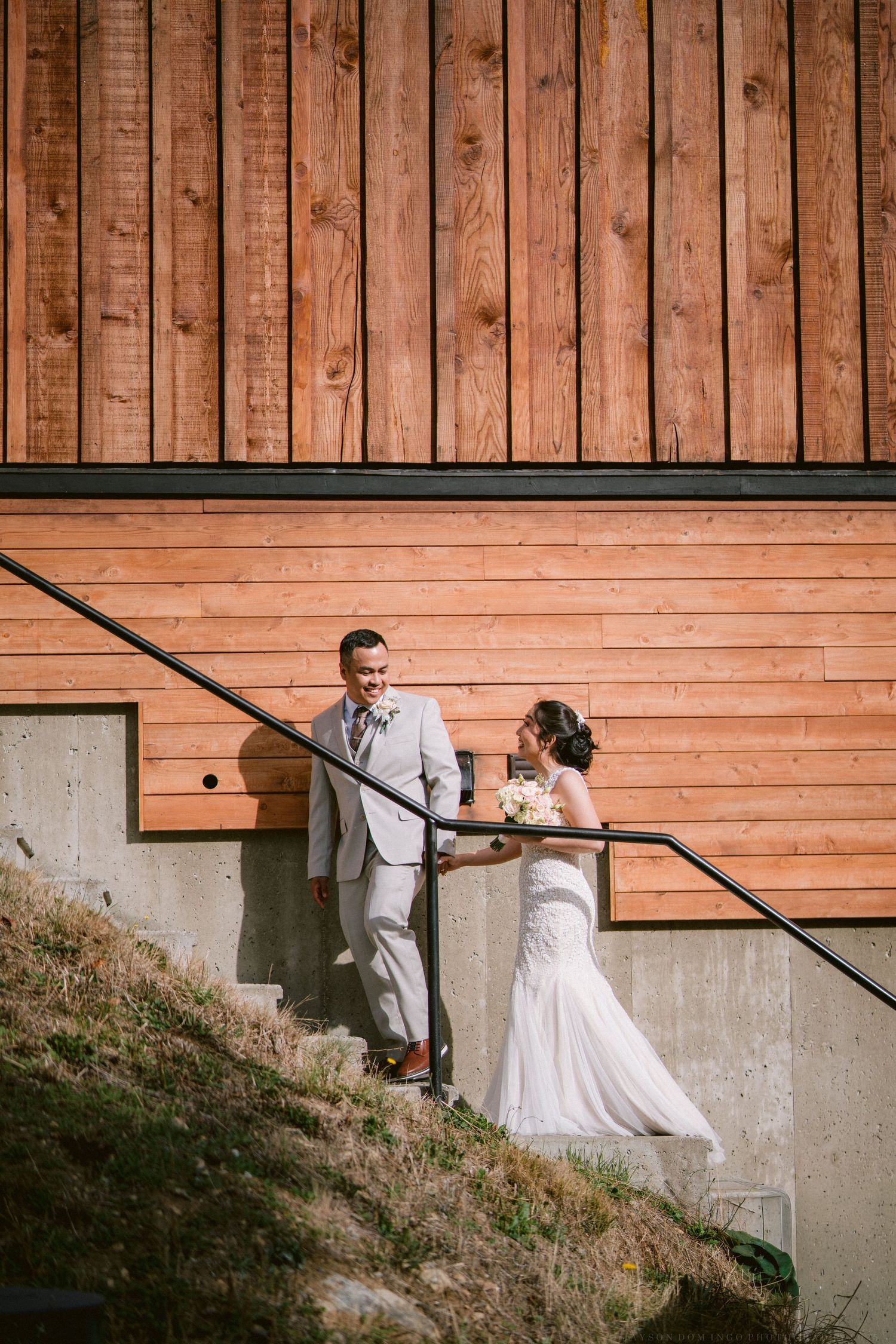 Wedding couple descending wooden stairs against rustic cedar siding in natural lighting.
