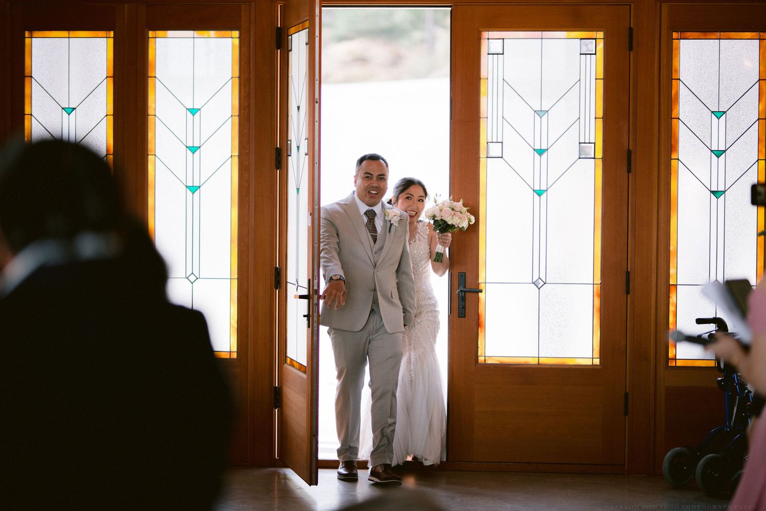 Silhouetted figures in formal attire against bright geometric windows in an indoor venue.