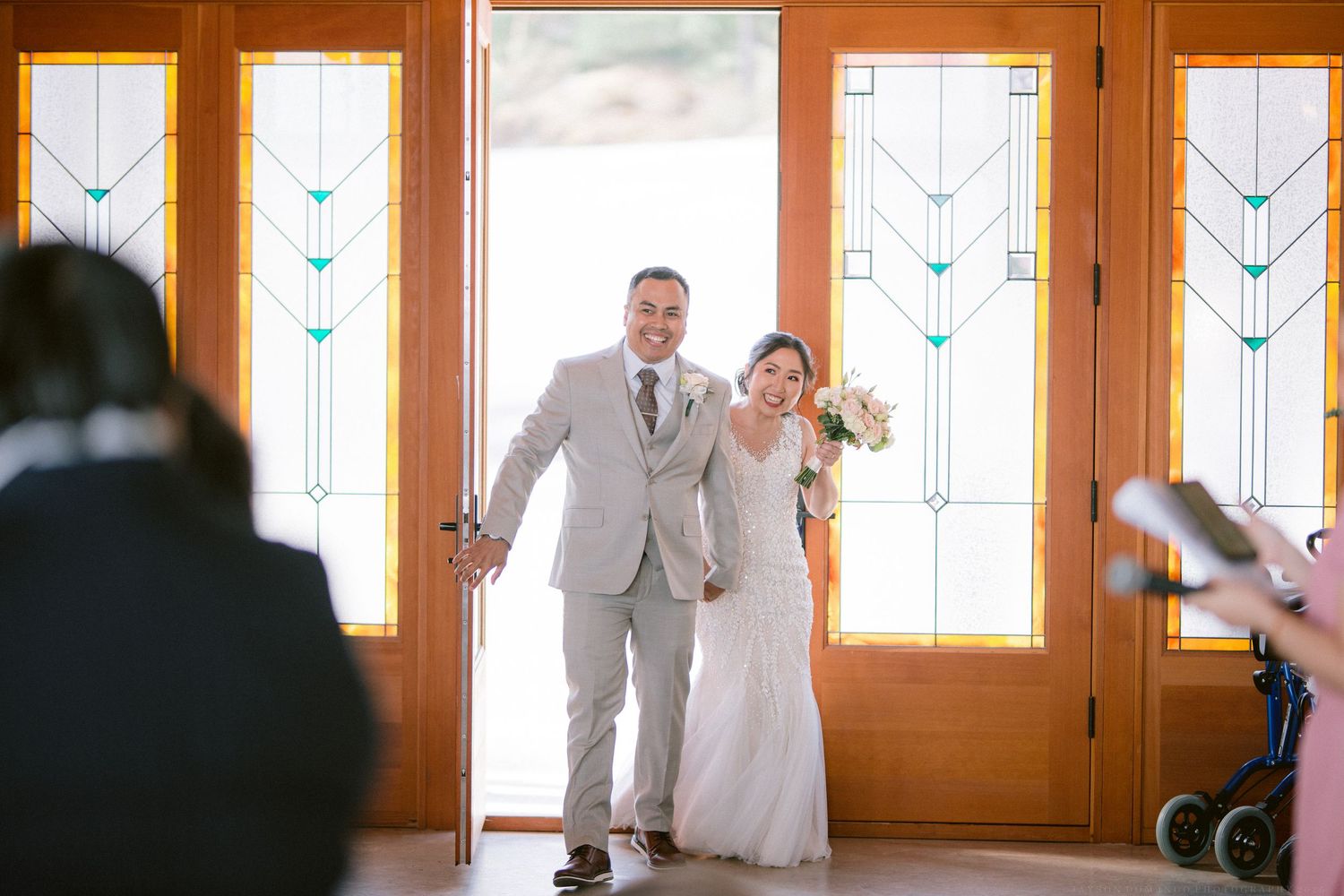 A couple makes their grand entrance through wooden doors with decorative stained glass panels.