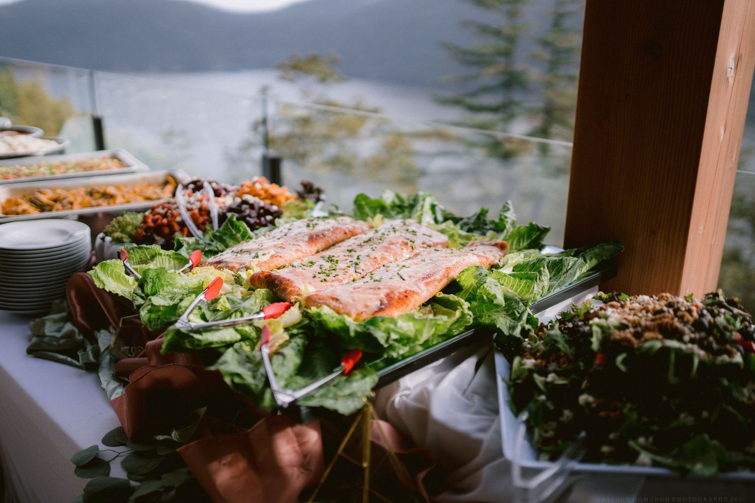 Fresh salmon fillets garnished with herbs and greens arranged on wooden serving boards for catering.