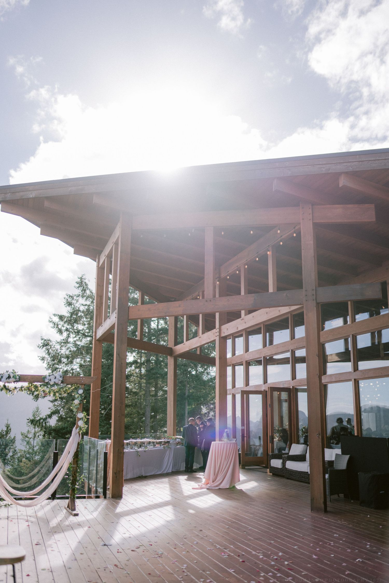 A panoramic view of a modern wooden deck venue with mountain views and string lights.