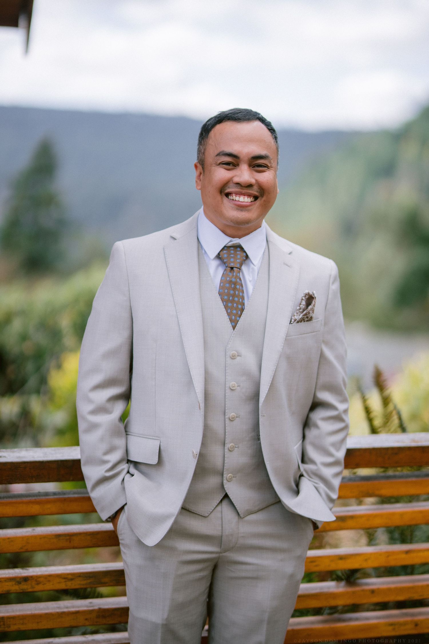 Wedding attire featuring a light beige three-piece suit with vest and patterned tie.