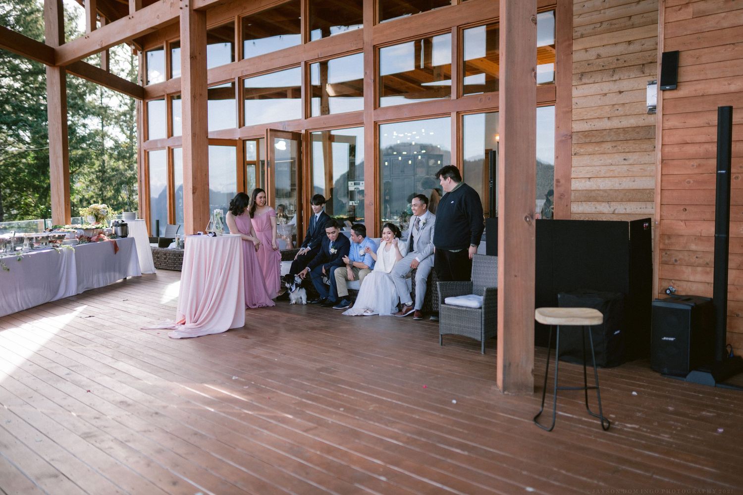 Wedding guests gather on a wooden deck with mountain views during an outdoor reception.