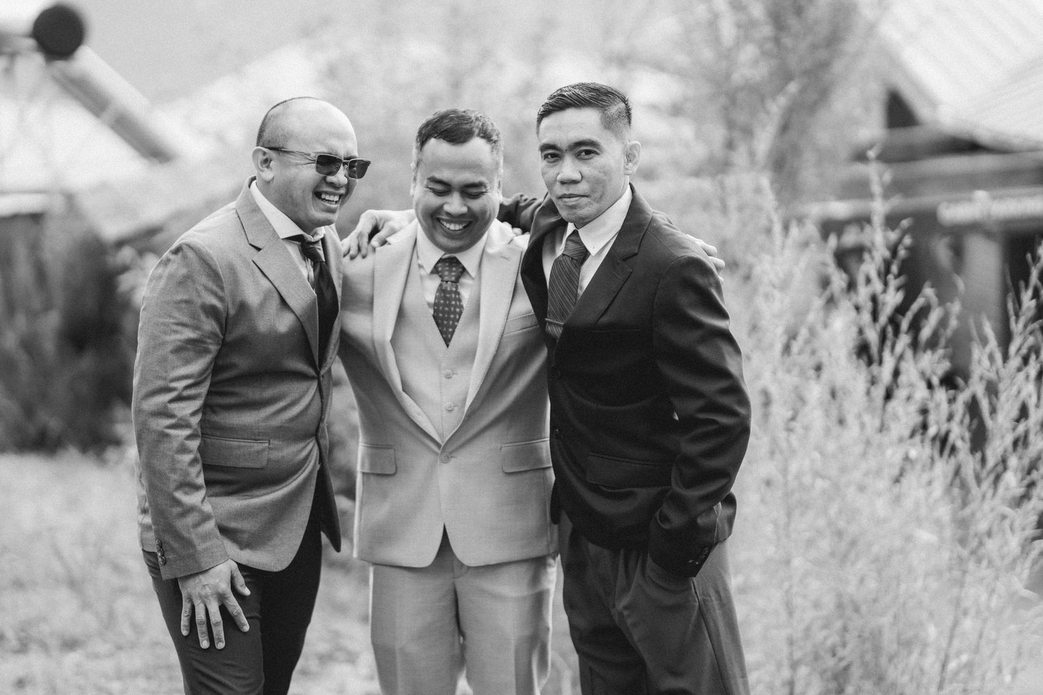 Candid black and white photo of groomsmen sharing a laugh outdoors.