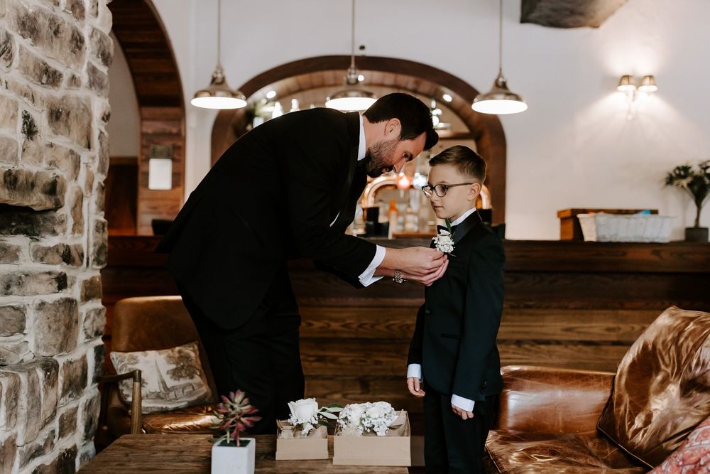 A touching moment between two people in formal attire standing in a stone-walled venue with wooden accents.