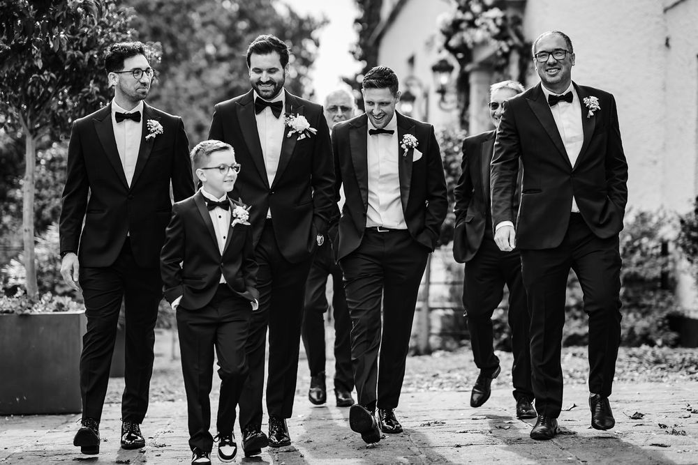 Groomsmen walking in a line wearing black tuxedos and bow ties on a wedding day.