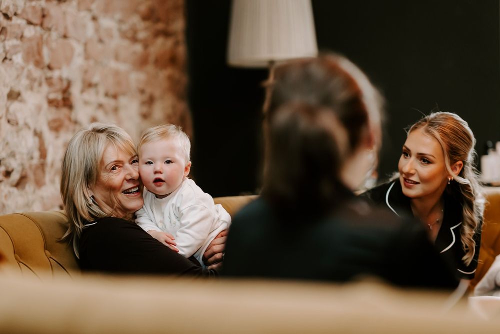 Three people share a candid moment while sitting on a tan leather couch in a rustic interior setting.