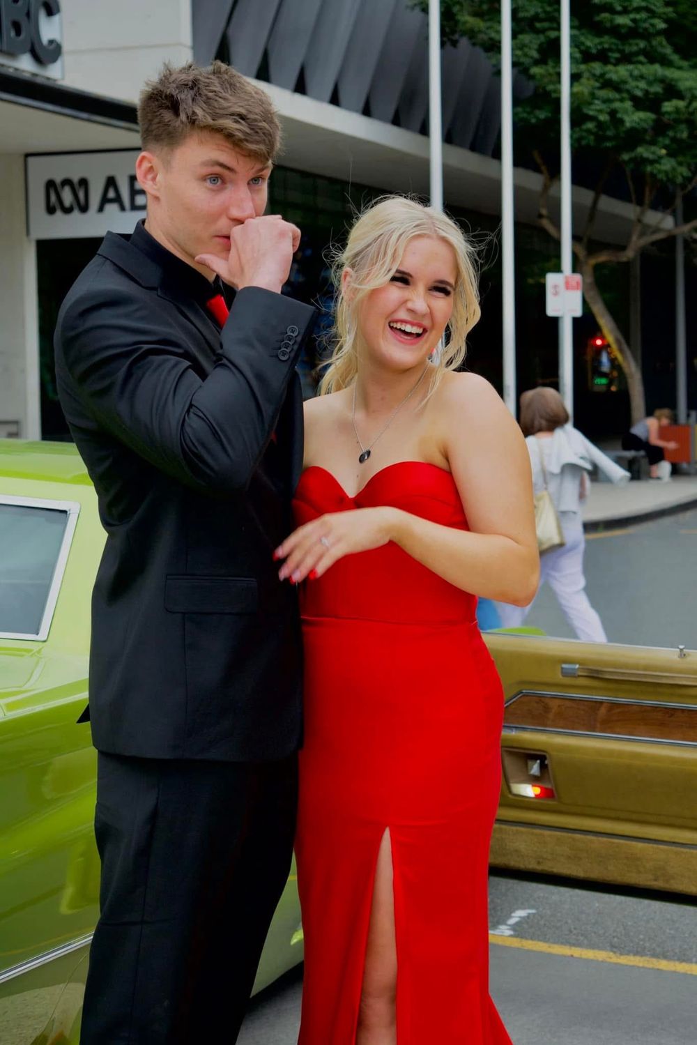 A couple in formal wear shares a lighthearted moment outside a building.