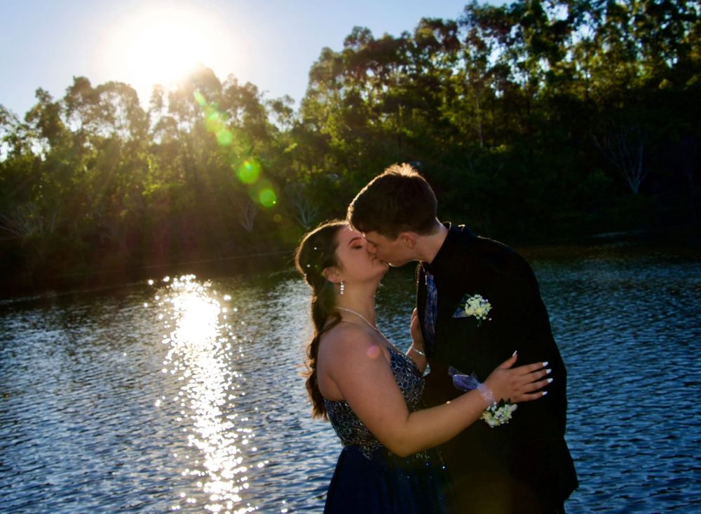 A couple shares a romantic moment at sunset by a lake with lens flare effects.