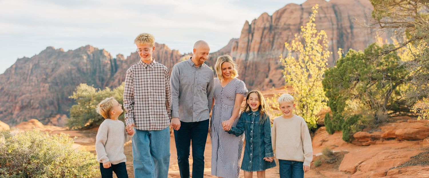 Extended family poses together against stunning red rock formations in Snow Canyon State Park at sunset.