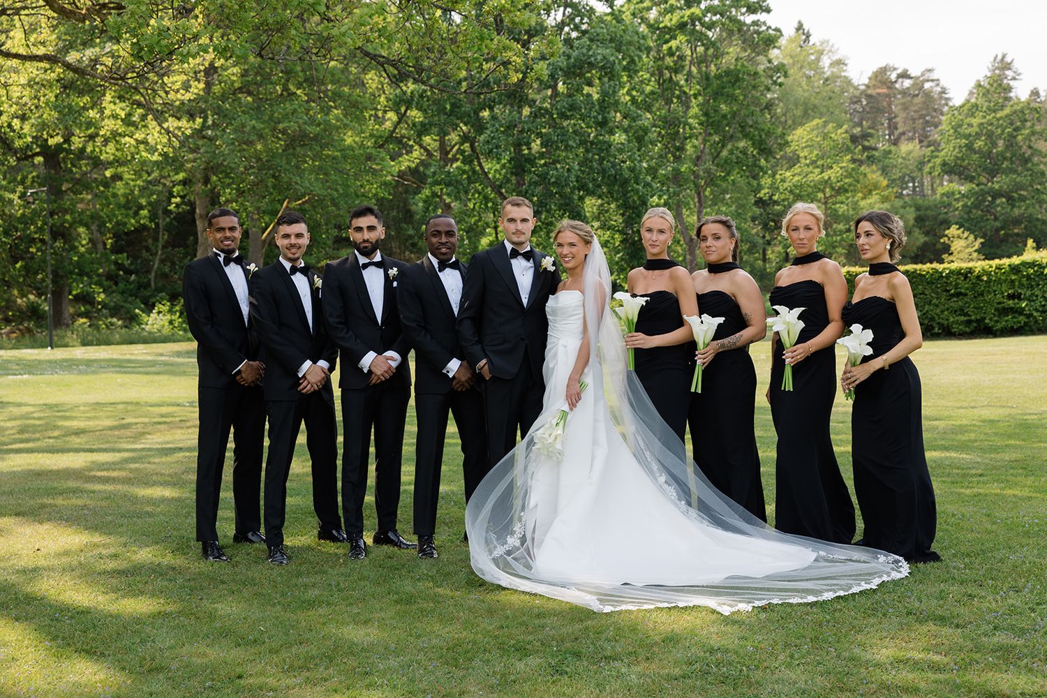 Wedding party poses together on a lush green lawn during an outdoor summer celebration.