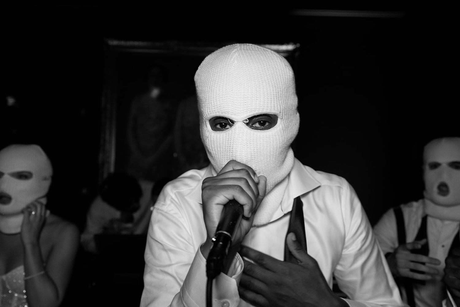 A group of people wearing white masks sit at a table in a dark room.