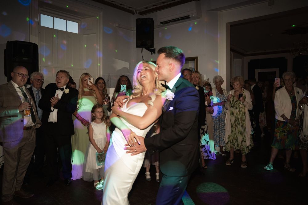 Couples dancing together at a wedding reception with colorful lighting and a crowded dance floor.