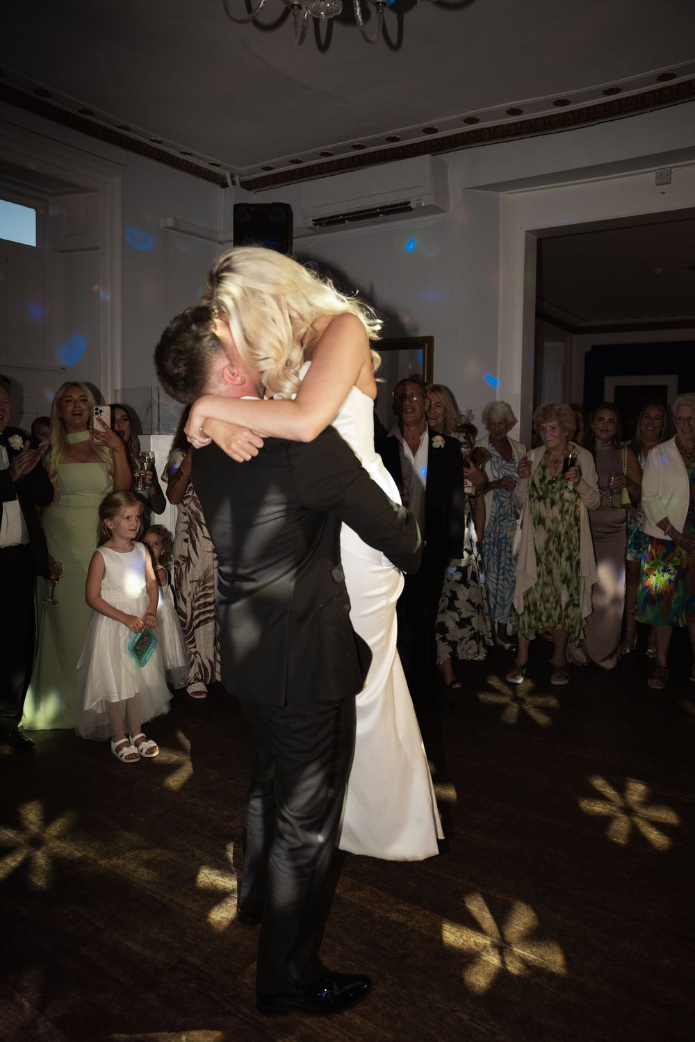 A couple performs an elegant dip during their first dance at a wedding reception while guests watch in the background.