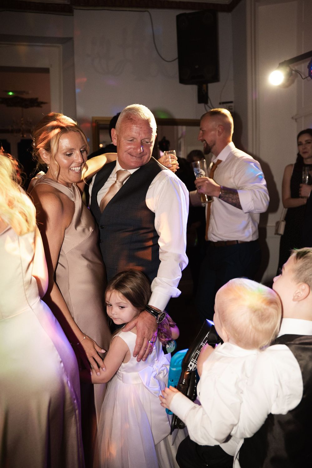 People dancing and celebrating at a wedding reception with a small child in a white dress on the dance floor.