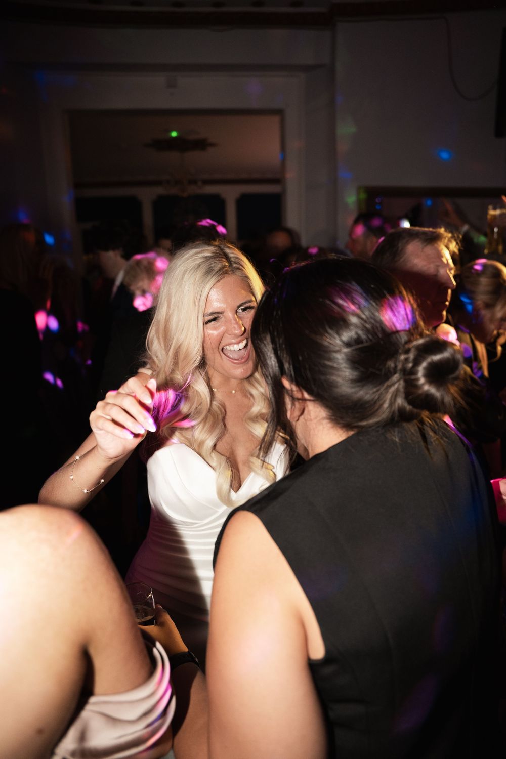 People dancing and celebrating at a wedding reception with colorful disco lights illuminating the dark room.