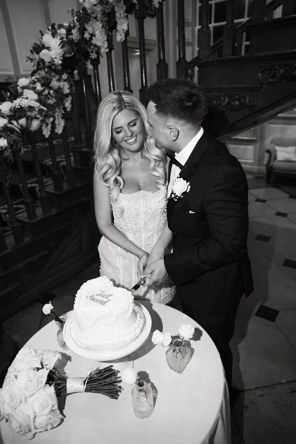 Black and white wedding photos show newlyweds sharing intimate moments during cake cutting at their reception.