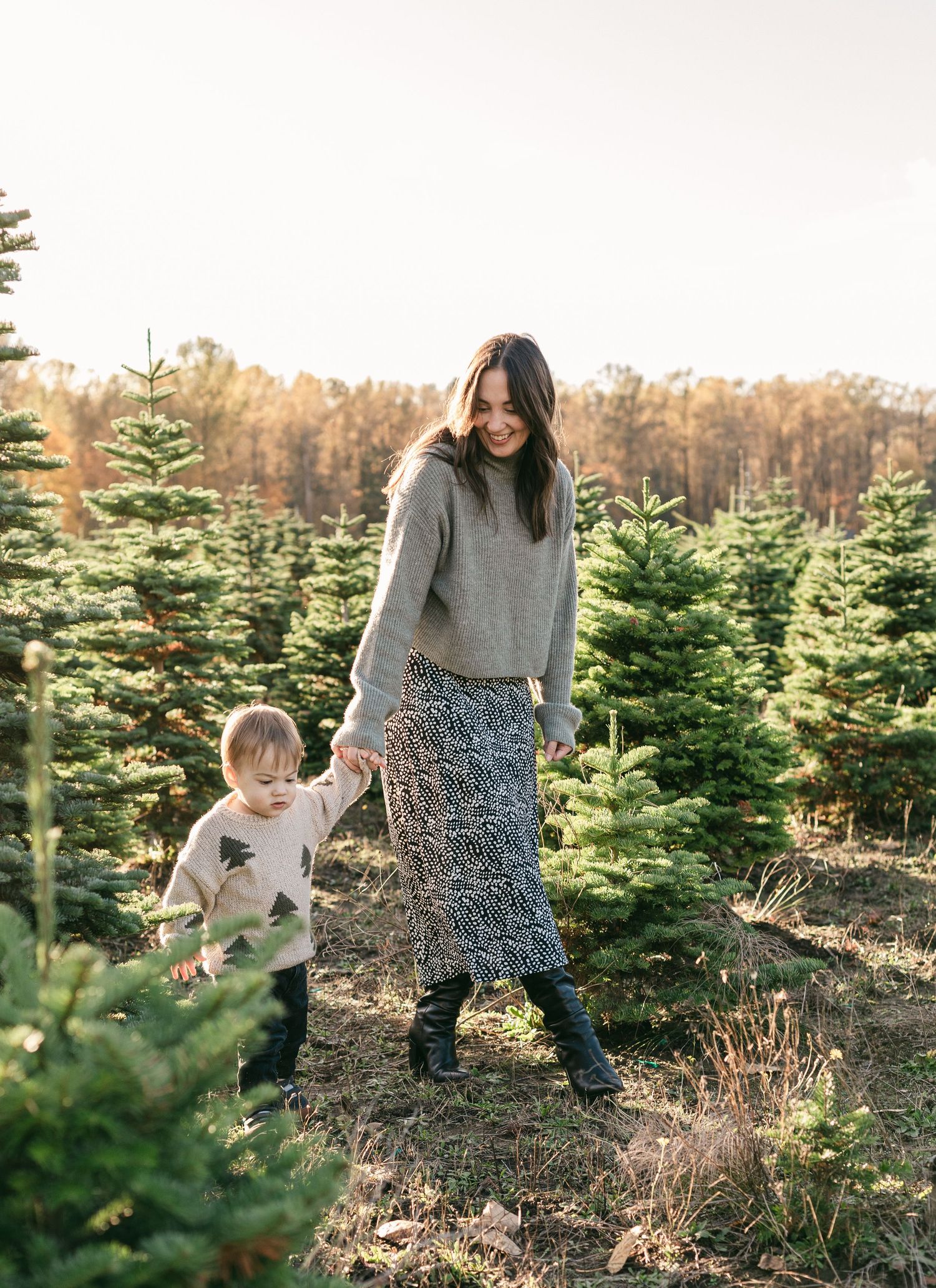 Mother and child explore a Christmas tree farm together on a sunny winter afternoon.
