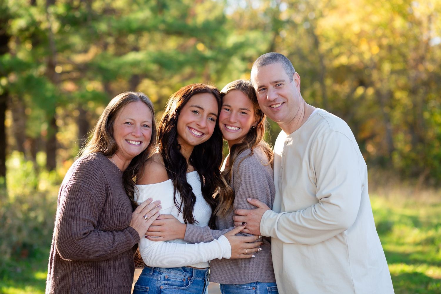 Group of people embracing and laughing together outdoors during autumn with golden foliage in background.