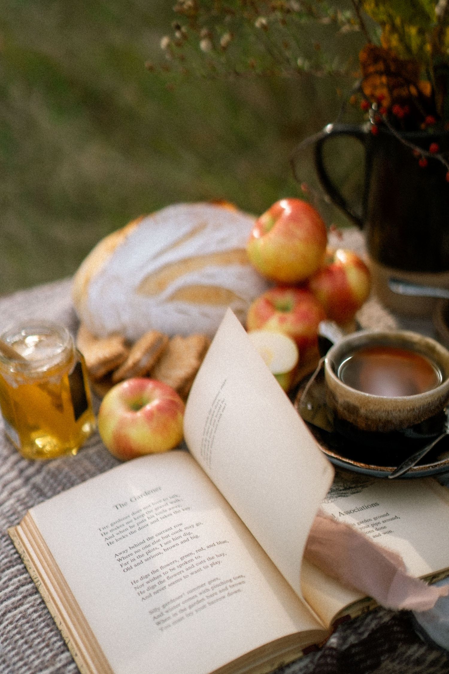 A cozy reading scene with an open book, apples, and steaming hot beverage against a soft blurred background.