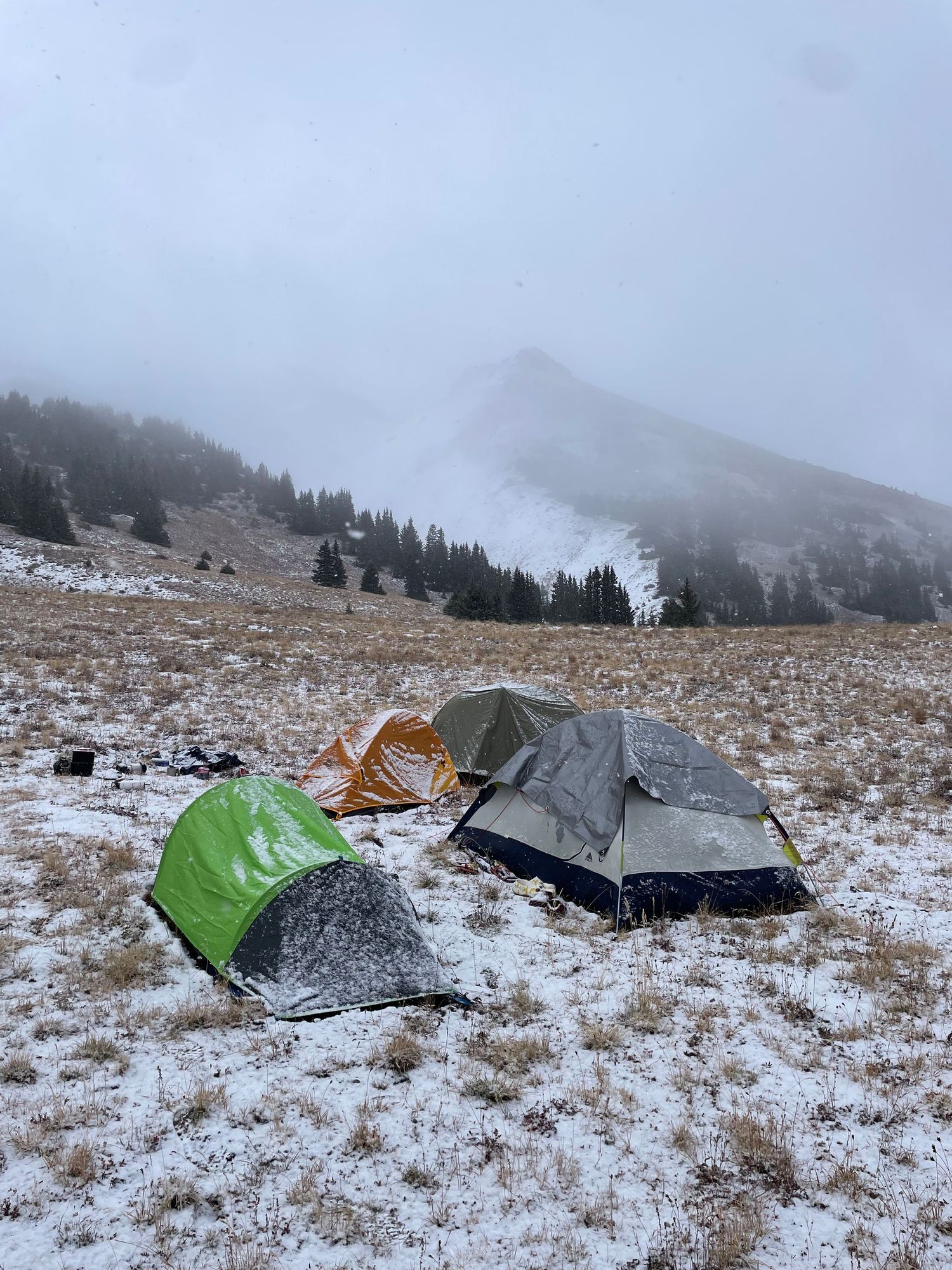 Damaged camping tents scattered across a snowy mountain landscape with misty peaks in the background.
