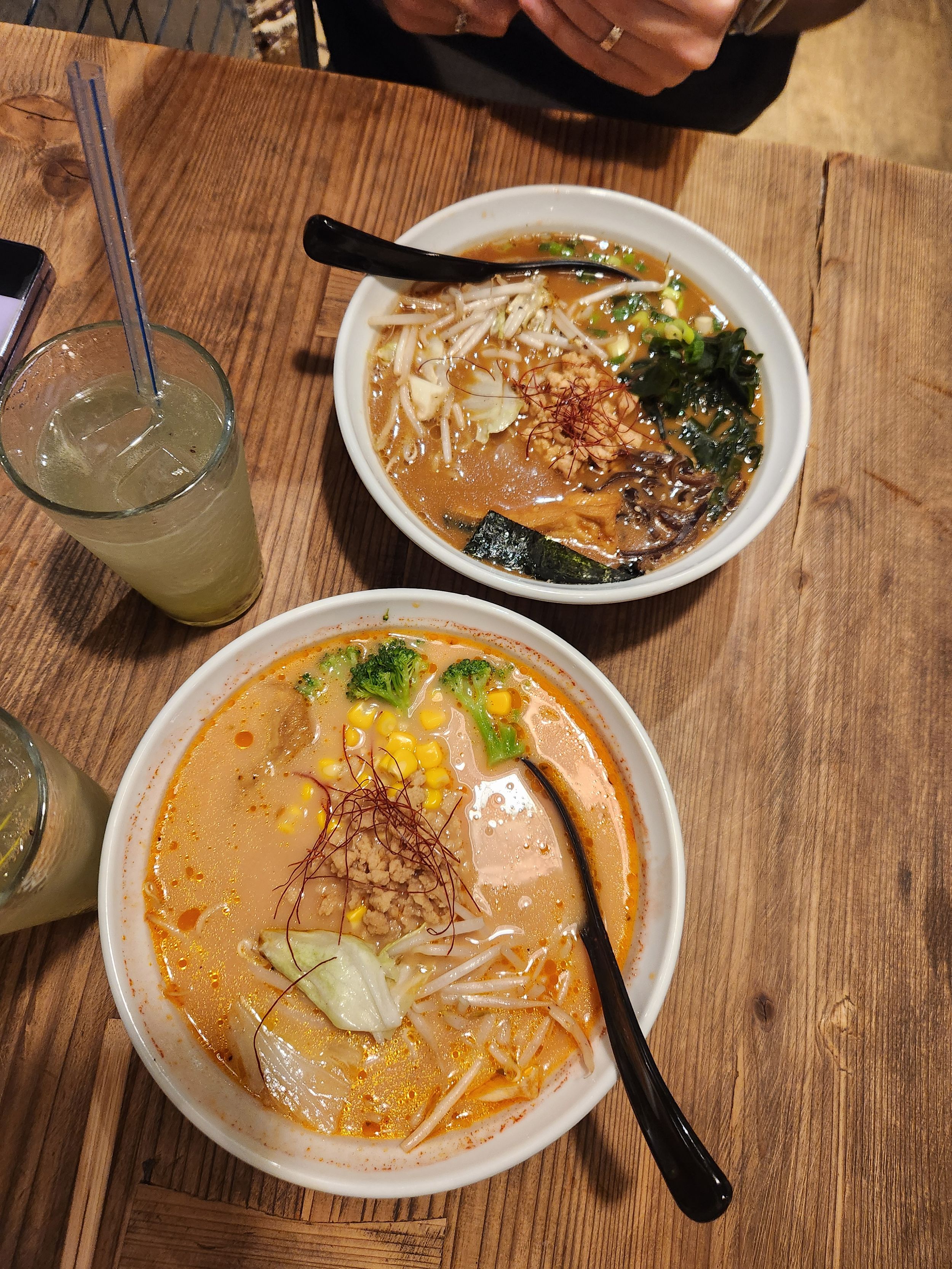Bowls of creamy ramen noodle soup with broth, vegetables and garnishes served on a rustic wooden table.