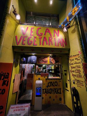 A narrow hallway with yellow walls features illuminated signs for vegan and vegetarian food options at a restaurant.