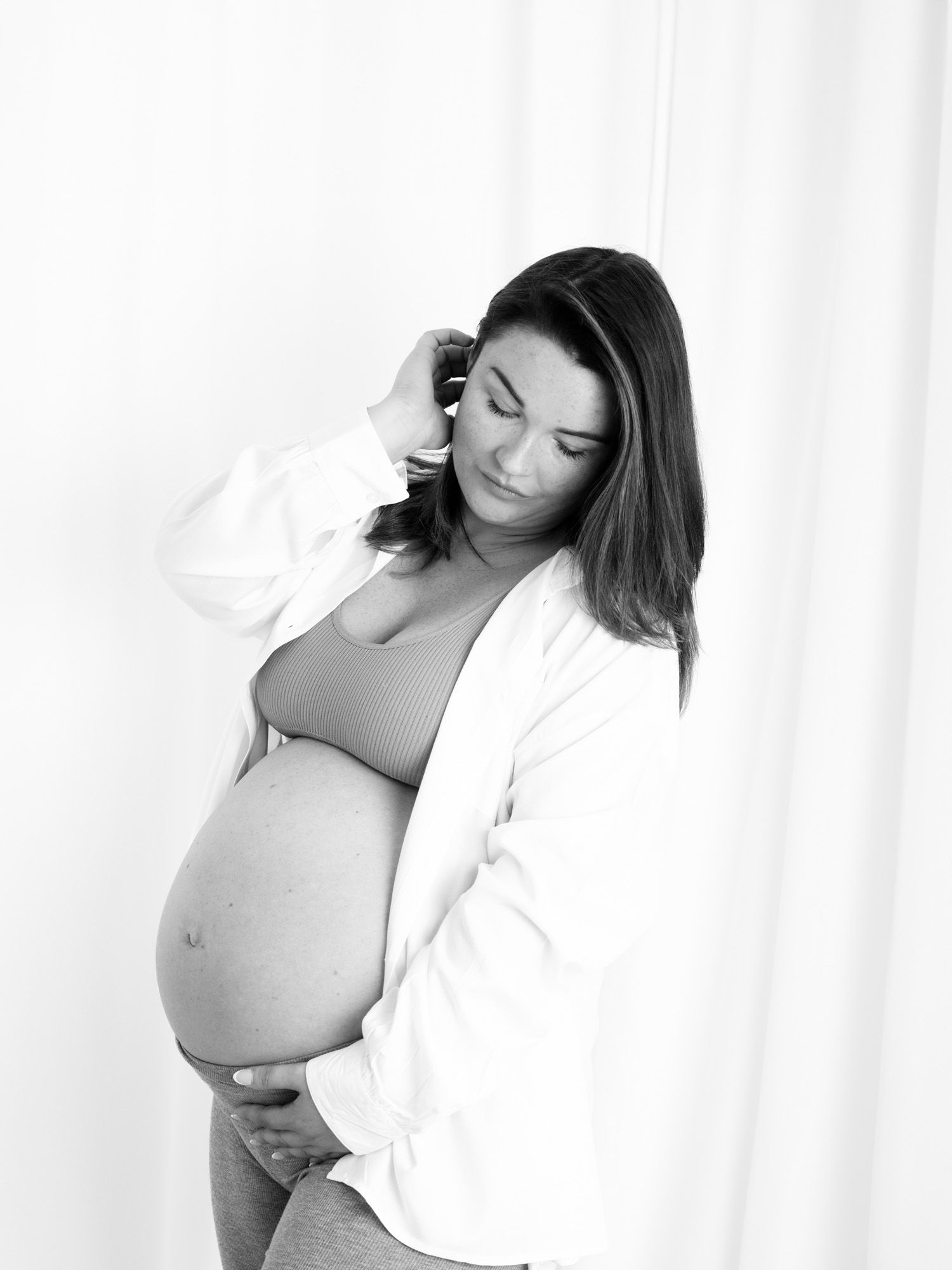 Black and white maternity photo series showing silhouette of pregnant woman in white shirt against light background.