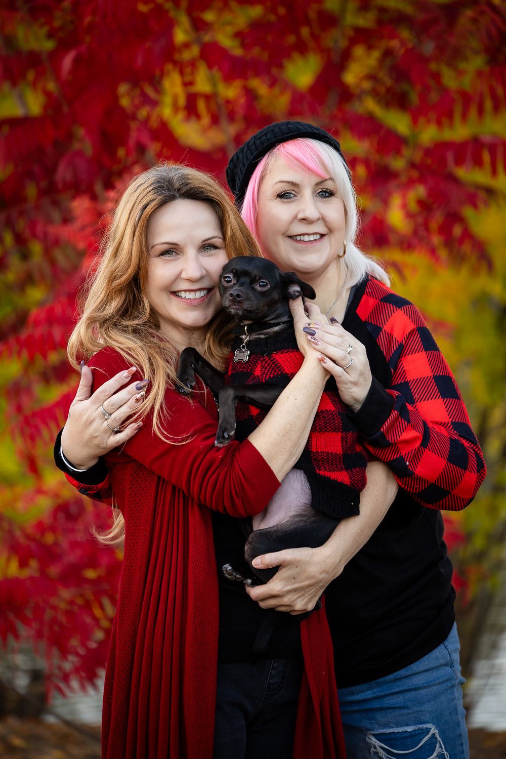 Sisters from San Jose pose with their dog in front of fall foliage
