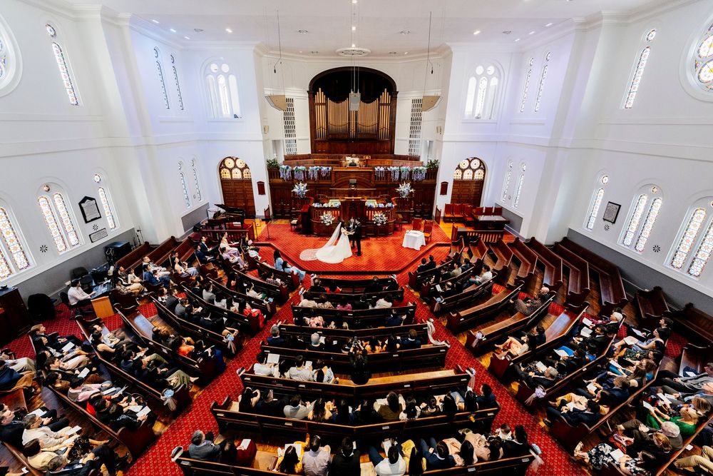 Interior panoramic view of a church sanctuary filled with people attending a worship service on red carpet.
